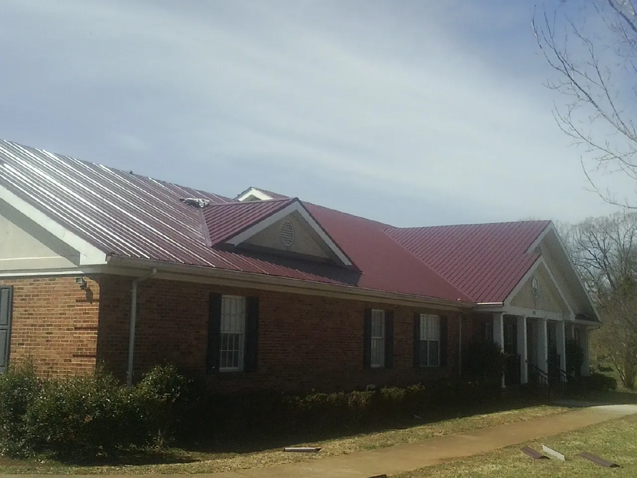 Red metal roof with gabled entries on a long brick building, from a Hail Damage Roof Repair job in Euless