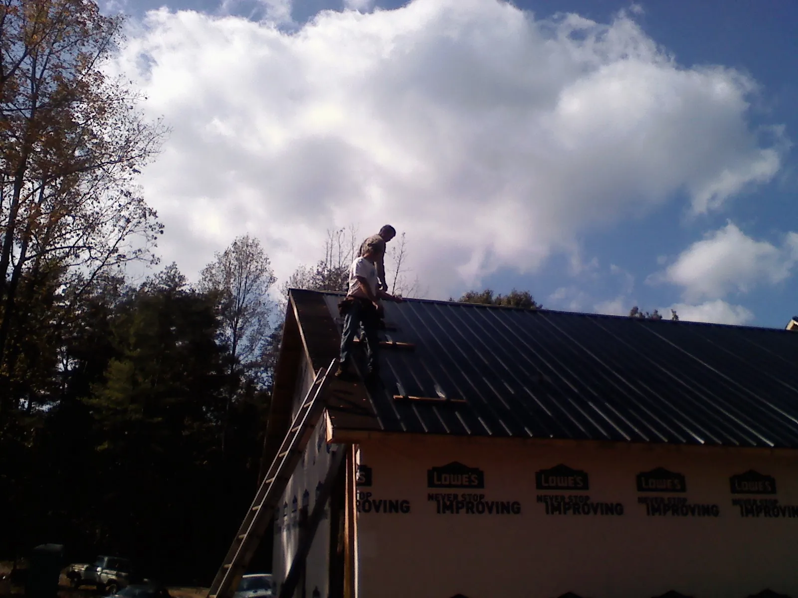Roofer fastening dark metal panels high against a cloudy sky, from a Roof Inspection job in Euless