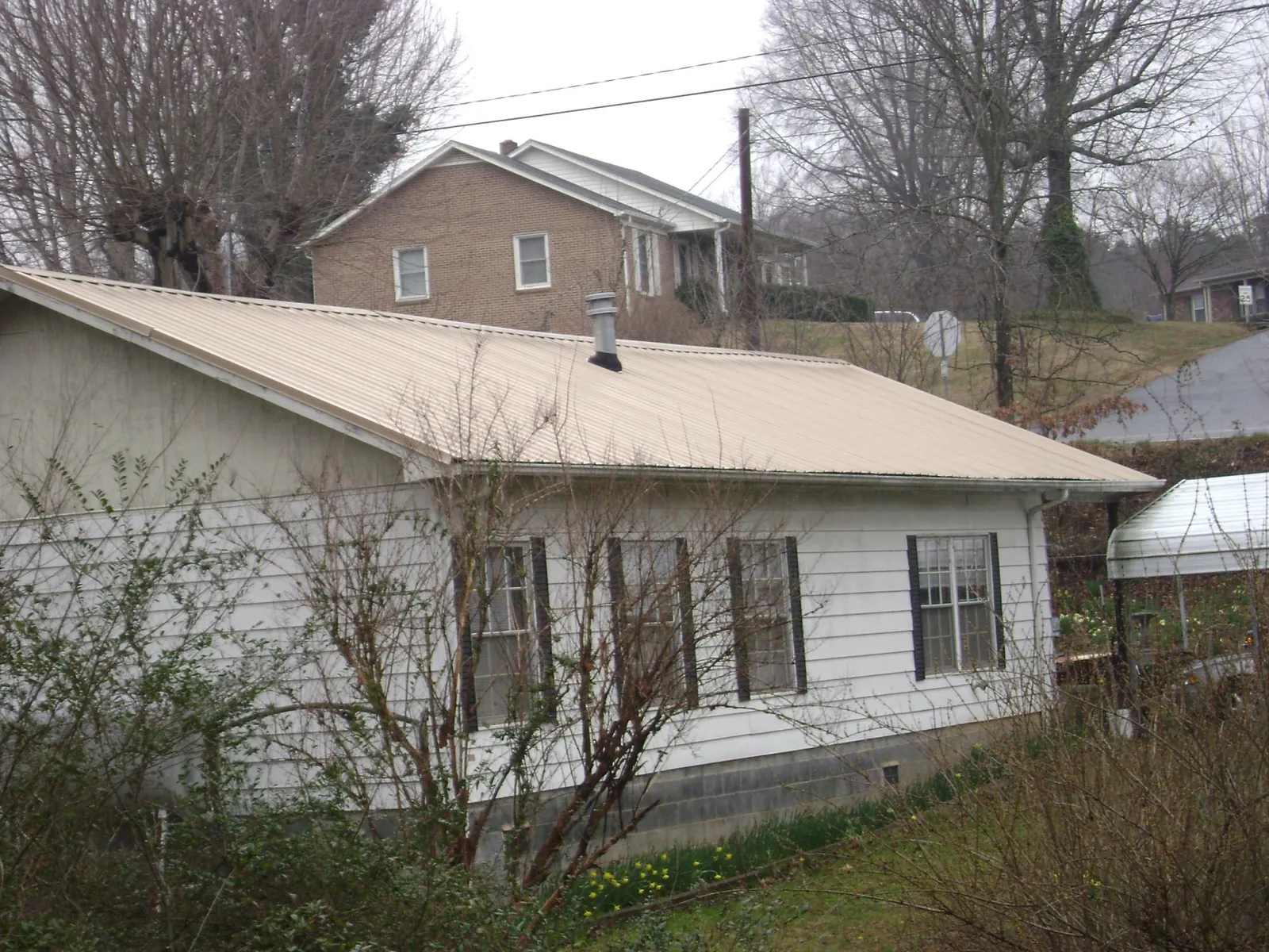 Tan metal roof on a white sided house set into a hillside — Commercial Roofing by Roofing Brothers in Euless